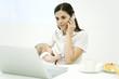 Woman nursing baby, using cell phone and looking at laptop