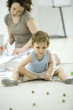 Photo: Boy playing with marbles while young mother uses phone and looks at paperwork in background Boy playing with marbles while young mother uses phone and looks at paperwork in background