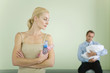 Photo: Woman holding baby bottles, looking over shoulder at husband holding baby in background Woman holding baby bottles, looking over shoulder at husband holding baby in background
