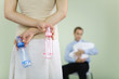 Photo: Woman holding baby bottles behind her back, husband holding baby in background, cropped view Woman holding baby bottles behind her back, husband holding baby in background, cropped view