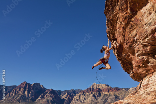 Photo: Female rock climber clinging to a cliff. Female rock climber clinging to a cliff.