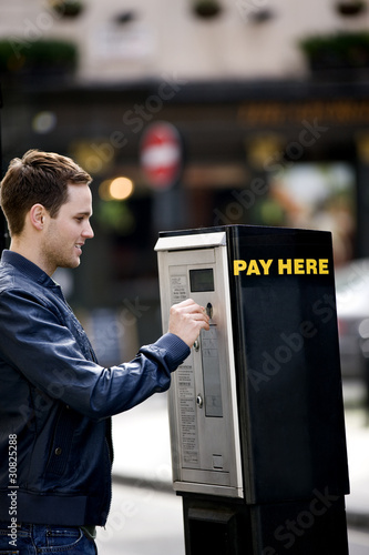 Photo: A young man putting coins in a parking meter A young man putting coins in a parking meter
