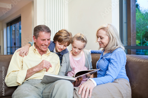 Photo: Grandparents and grandchildren on couch looking into book Grandparents and grandchildren on couch looking into book
