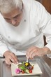 Mid- adult chef arranges edible flowers on salad