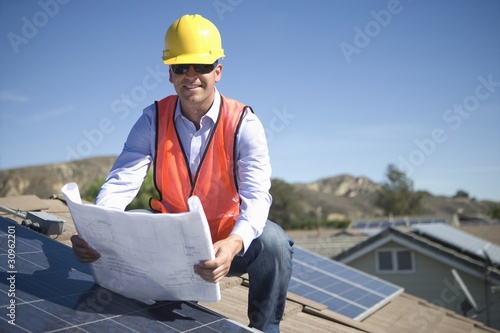 Photo: A business man on a solar panalled rooftop looking at plans A business man on a solar panalled rooftop looking at plans