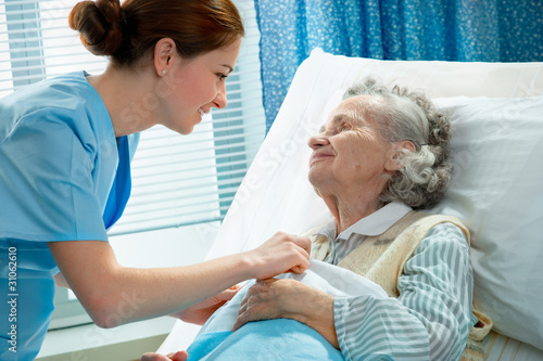 Photo: Nurse cares for a elderly woman lying in bed Nurse cares for a elderly woman lying in bed