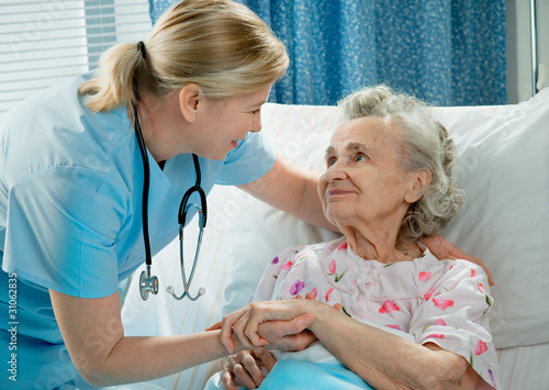 Photo: Nurse cares for a elderly woman lying in bed Nurse cares for a elderly woman lying in bed