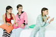 Photo: Three young female friends sitting on sofa, two watching younger girl putting on make-up Three young female friends sitting on sofa, two watching younger girl putting on make-up