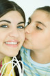 Two young female friends, one kissing the other on the cheek