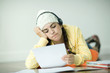 Young woman lying on floor listening to headphones and doing homework