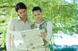 Couple standing outdoors, reading newspaper