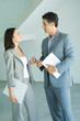 Photo: Well dressed man and woman standing in bare home interior, speaking, woman holding binder, man holding blueprints Well dressed man and woman standing in bare home interior, speaking, woman holding binder, man holding blueprints