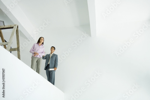 Photo: Young woman standing with architect, looking over unfinished interior, low angle view Young woman standing with architect, looking over unfinished interior, low angle view