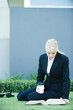 Photo: Young businesswoman sitting on the ground outdoors, reading book, holding hot beverage Young businesswoman sitting on the ground outdoors, reading book, holding hot beverage