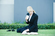 Photo: Young businesswoman sitting on the ground outdoors, reading book, holding hot beverage Young businesswoman sitting on the ground outdoors, reading book, holding hot beverage