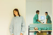Photo: Medical workers chatting in office, one lying down on bench, female patient standing in foreground Medical workers chatting in office, one lying down on bench, female patient standing in foreground