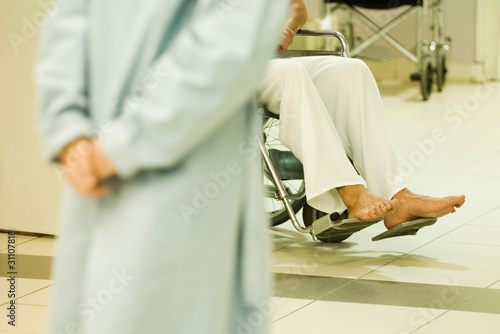 Photo: Patient sitting in wheel chair, cropped view, adult with clasped hands in foreground Patient sitting in wheel chair, cropped view, adult with clasped hands in foreground
