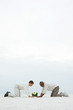 Photo: Two men down on all fours in sand, both looking down at flower growing out of wheat grass Two men down on all fours in sand, both looking down at flower growing out of wheat grass