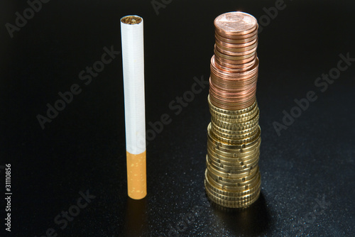 Photo: Cigarette next to stack of coins, close-up Cigarette next to stack of coins, close-up