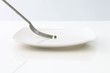 Fork approaching single pea on plate