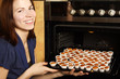 young housewife taking cupcakes from oven and smiling