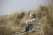 A senior woman sitting amongst the sand dunes, thinking