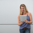 Smiling blond woman using electronic tablet on grey background