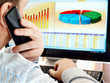 Man on a phone analyzing financial data and charts on computer Man on a phone analyzing financial data and charts on computer
