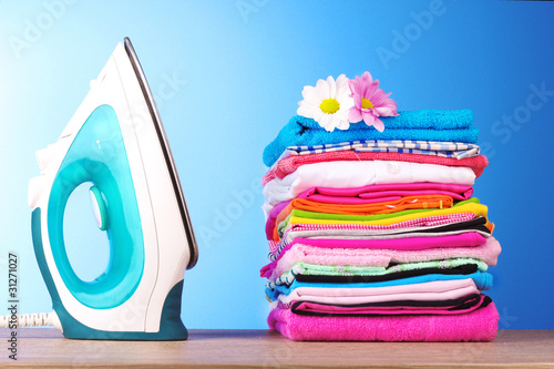 Photo: Pile of colorful clothes and electric iron on blue background Pile of colorful clothes and electric iron on blue background
