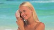 Blonde woman listening  to a shell