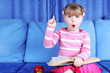 surprised little girl with apple and books in sofa