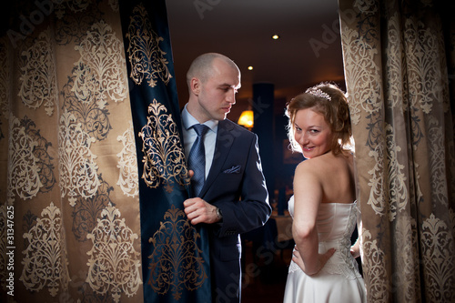 Photo: Wedding couple behind golden curtains in luxury interior. Wedding couple behind golden curtains in luxury interior.