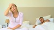Young woman on bed with headache while husband sleeps