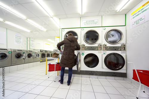 Photo: woman put laundry in washing machine in public laundry woman put laundry in washing machine in public laundry
