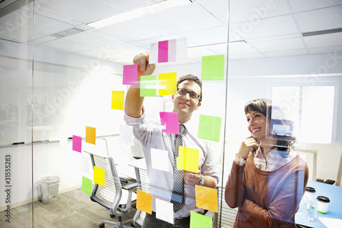 Photo: Business people looking at adhesive notes in conference room Business people looking at adhesive notes in conference room