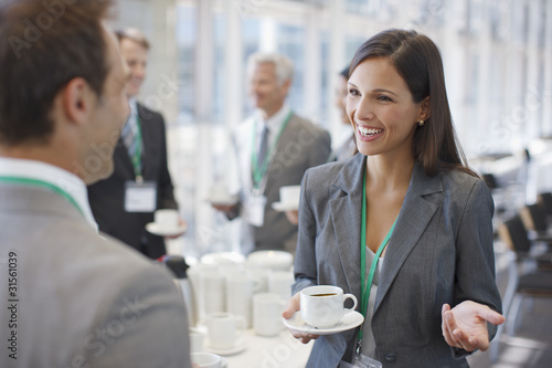 Photo: Businesswoman drinking coffee and talking to co-worker Businesswoman drinking coffee and talking to co-worker