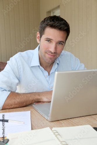 Photo: Smiling man working at home on laptop computer Smiling man working at home on laptop computer