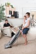 A Mother Trying To Vacuum While The Father Sits Around