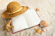 Book with straw hat and seashells in sand Book with straw hat and seashells in sand