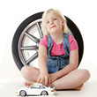 Foto: Cute blond girl playing with a toy car in front of a tyre Cute blond girl playing with a toy car in front of a tyre