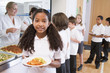 Schoolgirl holding plate of lunch in school cafeteria