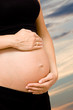 hands holding pregnant tummy with sky in the background