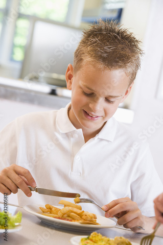 Photo: Schoolboy enjoying his lunch in a school cafeteria Schoolboy enjoying his lunch in a school cafeteria