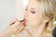 Young beautiful bride applying wedding make-up by make-up artist