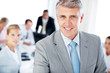 Photo: Smiling mature businessman with people working at the back Smiling mature businessman with people working at the back