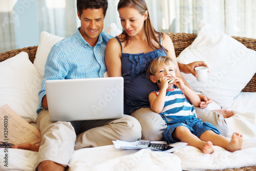 Photo: Couple using laptop with son eating watermelon Couple using laptop with son eating watermelon