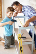 Little kid learning to use drill machine from his father