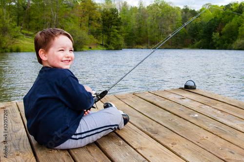 Photo: Boy smiles while fishing from dock on lake. Boy smiles while fishing from dock on lake.