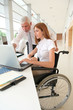 Photo: Woman in wheelchair with trainer in office Woman in wheelchair with trainer in office