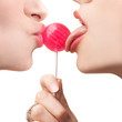 Two beautiful women licking and kissing a red lollipop against w